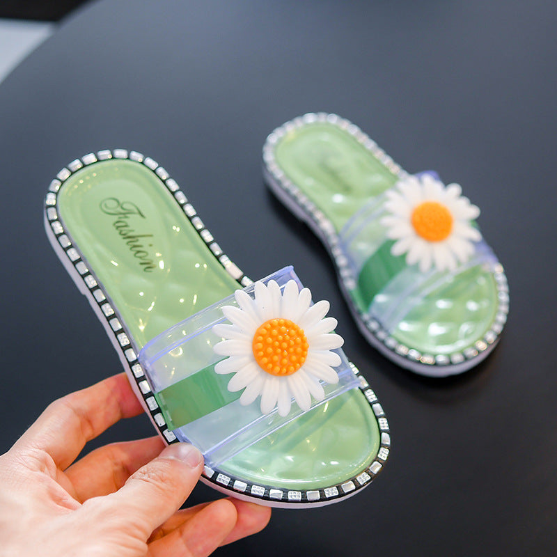 Green slide sandals with flower decorations held by a hand on a dark surface