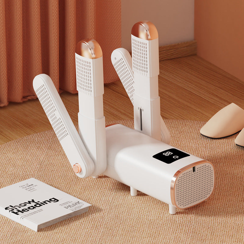 White and rose gold shoe dryer on a wooden floor with a book and shoes in the background