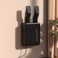 Black wall-mounted hair dryer with two nozzles on a beige wall.