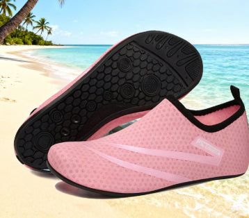 Pink and black water shoes on a beach with palm trees and blue sky.