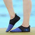Black and blue water shoes worn on feet with a blurred beach background
