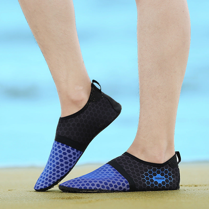 Black and blue water shoes worn on feet with a blurred beach background