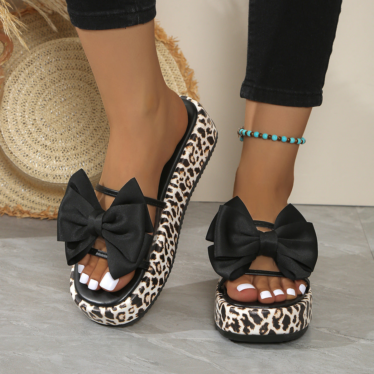 Leopard print sandals with black bows worn by a person on a neutral background