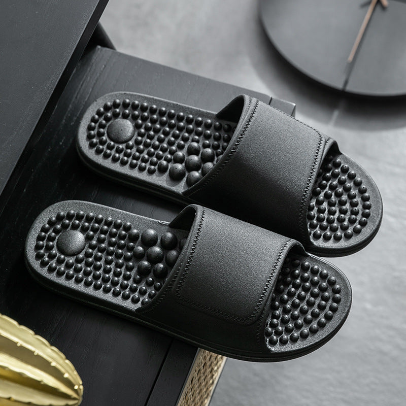 Black massage slippers on a dark surface with a clock in the background
