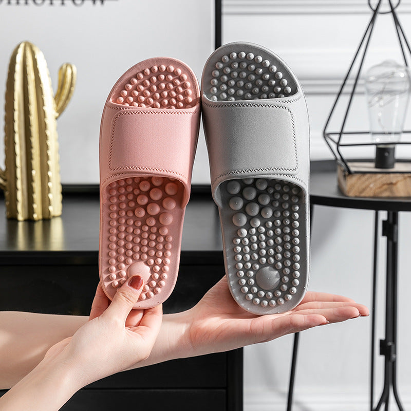 Pink and gray massage slippers held in a hand with a blurred indoor background