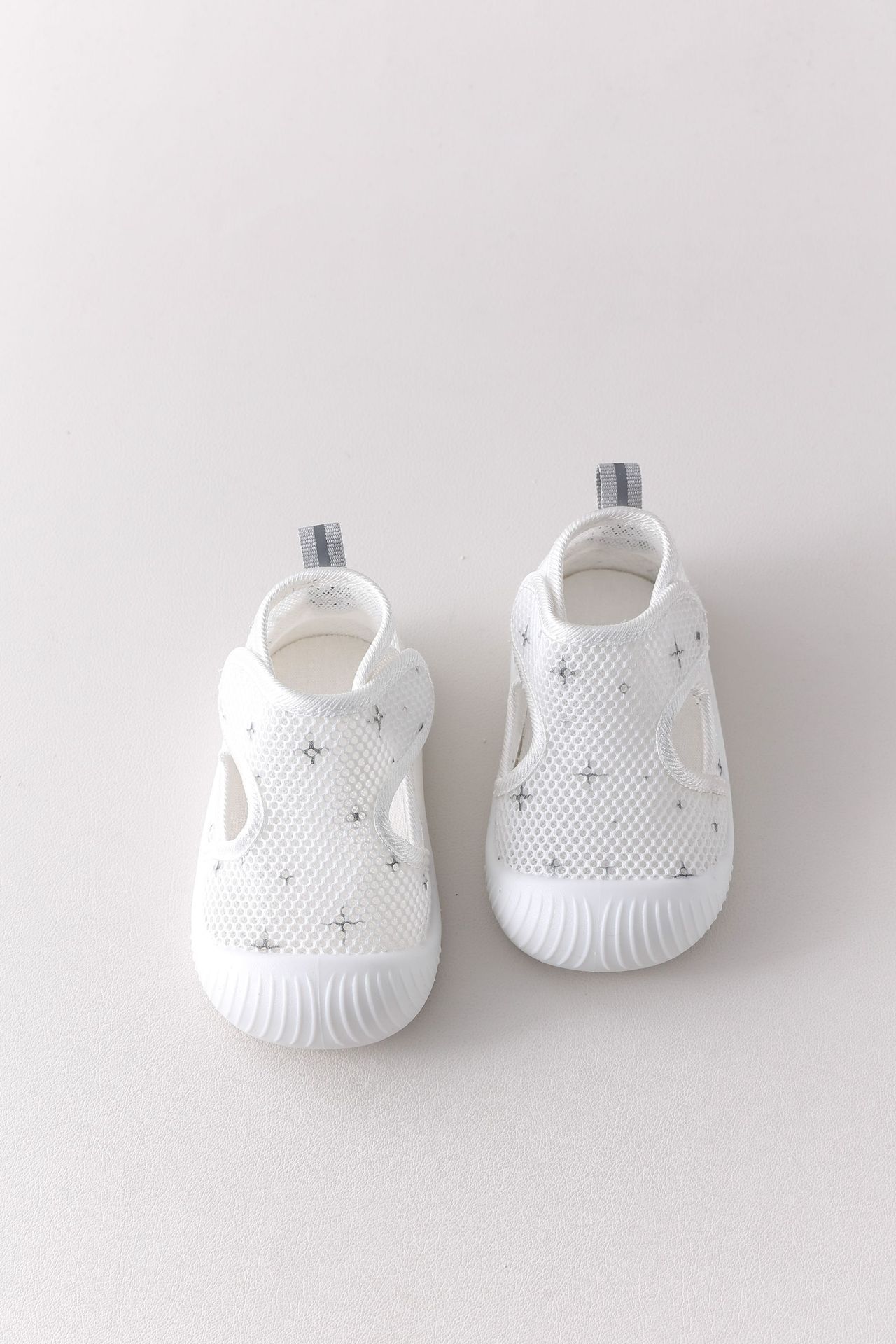Pair of white baby shoes with star patterns on a light gray background