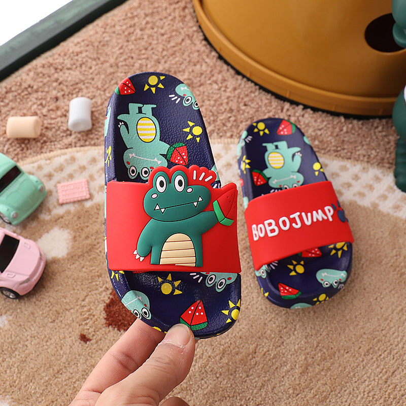 Children's sandals with a dinosaur design held by a hand on a carpeted floor.
