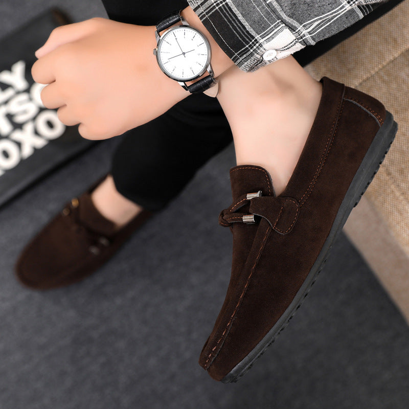 Brown loafers worn with a checkered shirt and black pants, sitting on a textured surface.