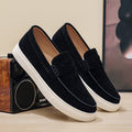 Black loafers with white soles on a wooden surface with a blurred background