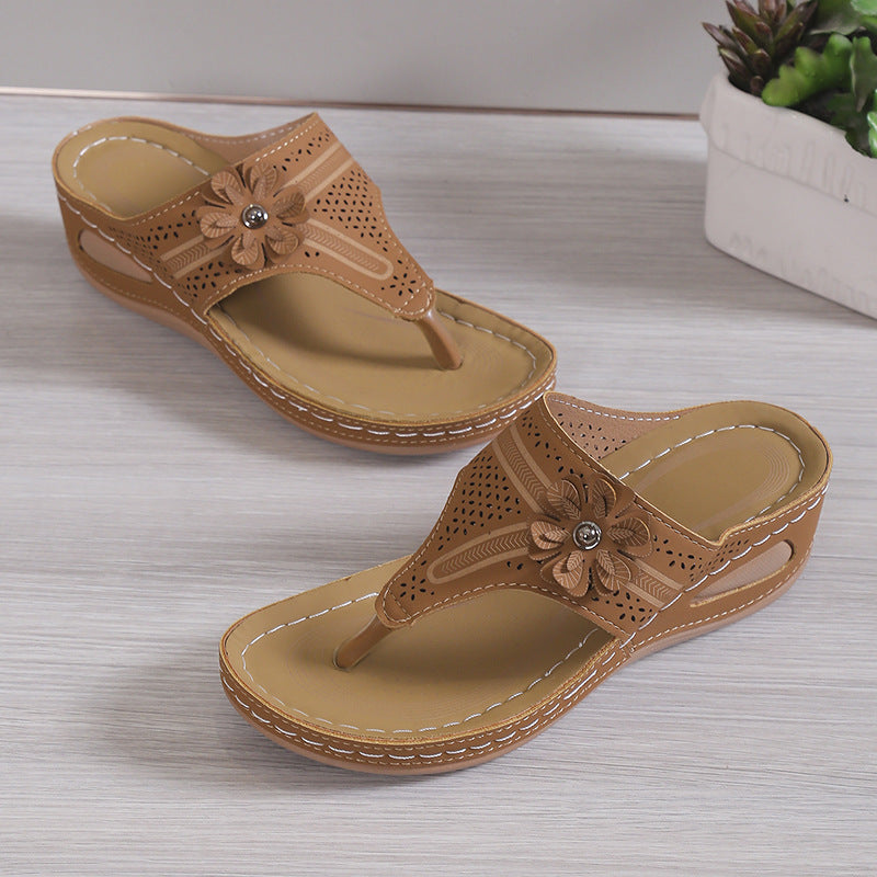 Pair of tan sandals with floral design on a light wooden surface.