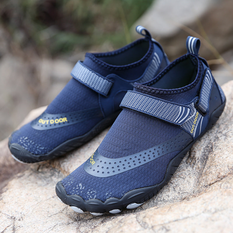 Pair of navy blue water shoes with velcro straps on a rock surface