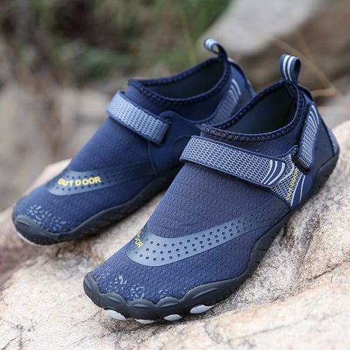 Pair of navy blue water shoes with velcro straps on a rock surface