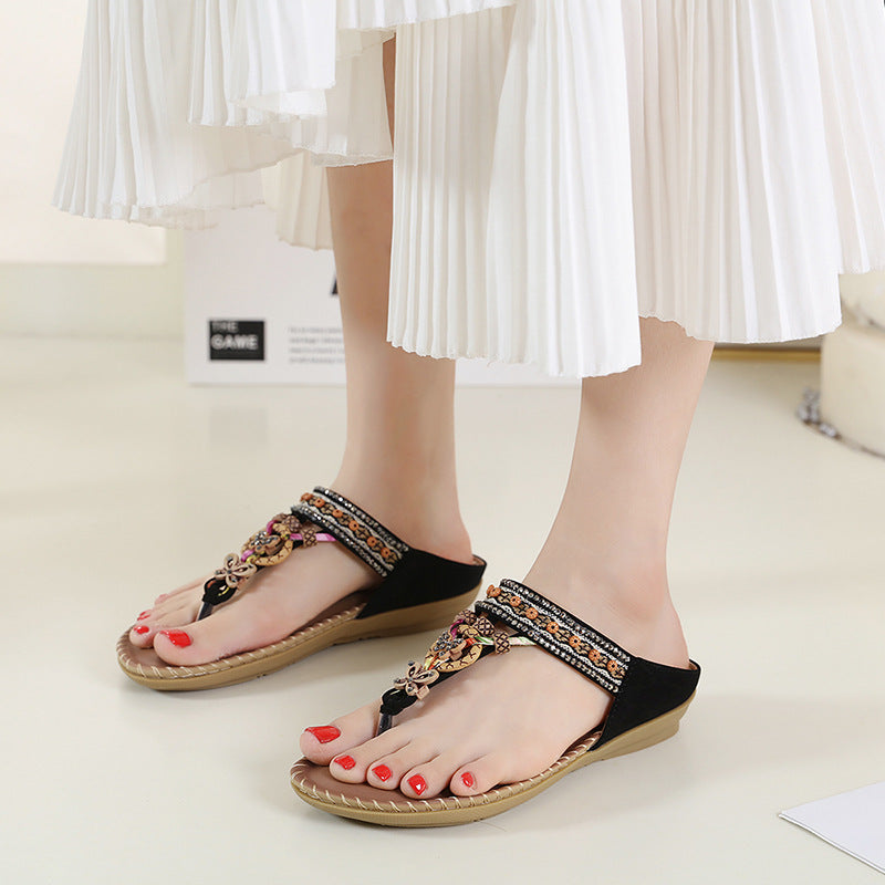 Black sandals with decorative straps worn by a person on a light background