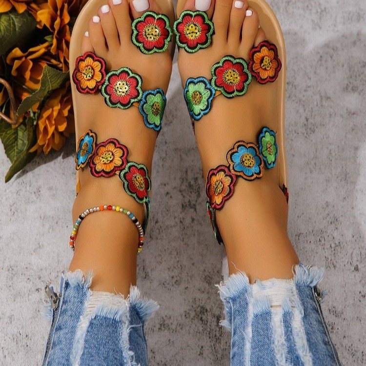 Colorful floral sandals worn with ripped jeans on a textured surface.
