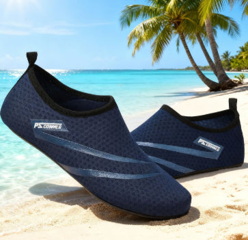 Navy blue water shoes on a sandy beach with palm trees and clear blue water in the background