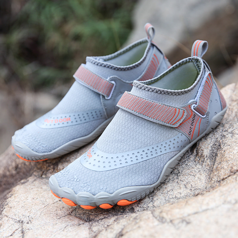 Pair of gray and pink shoes with orange soles on a rock surface