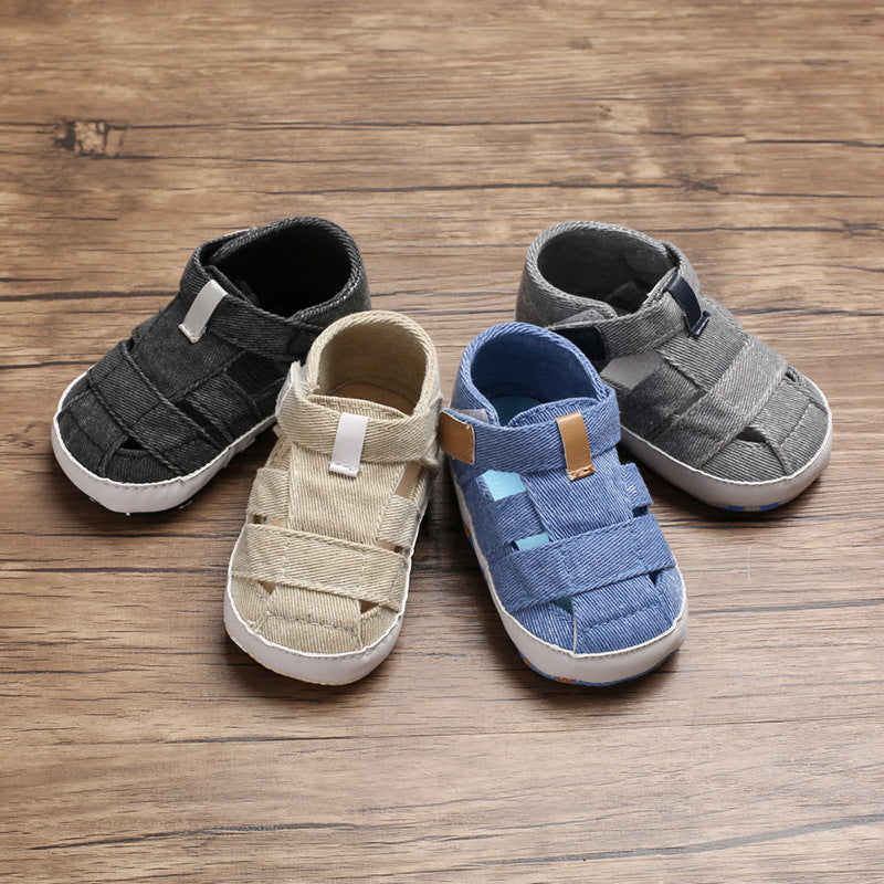 Four pairs of children's sandals in black, beige, blue, and gray on a wooden surface.