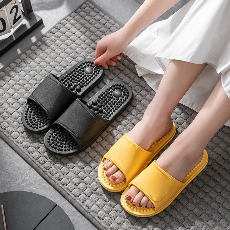 Person wearing black and yellow massage slippers on a textured floor.