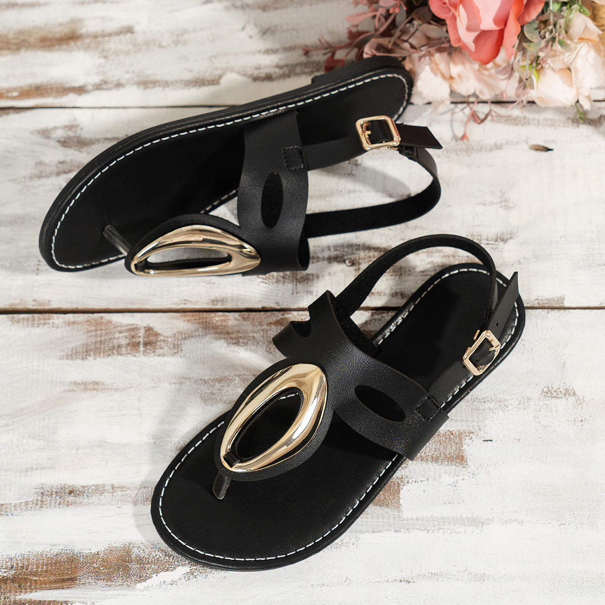 Black sandals with gold accents on a wooden surface