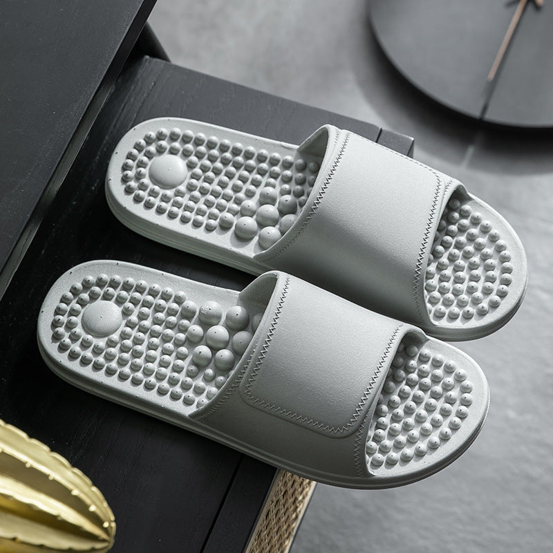 Gray massage slippers on a dark surface with a clock in the background