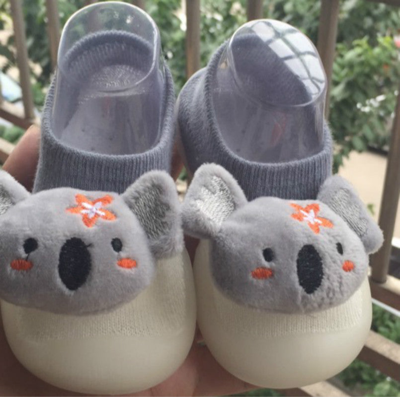 Pair of baby shoes with koala design held by a hand outdoors.