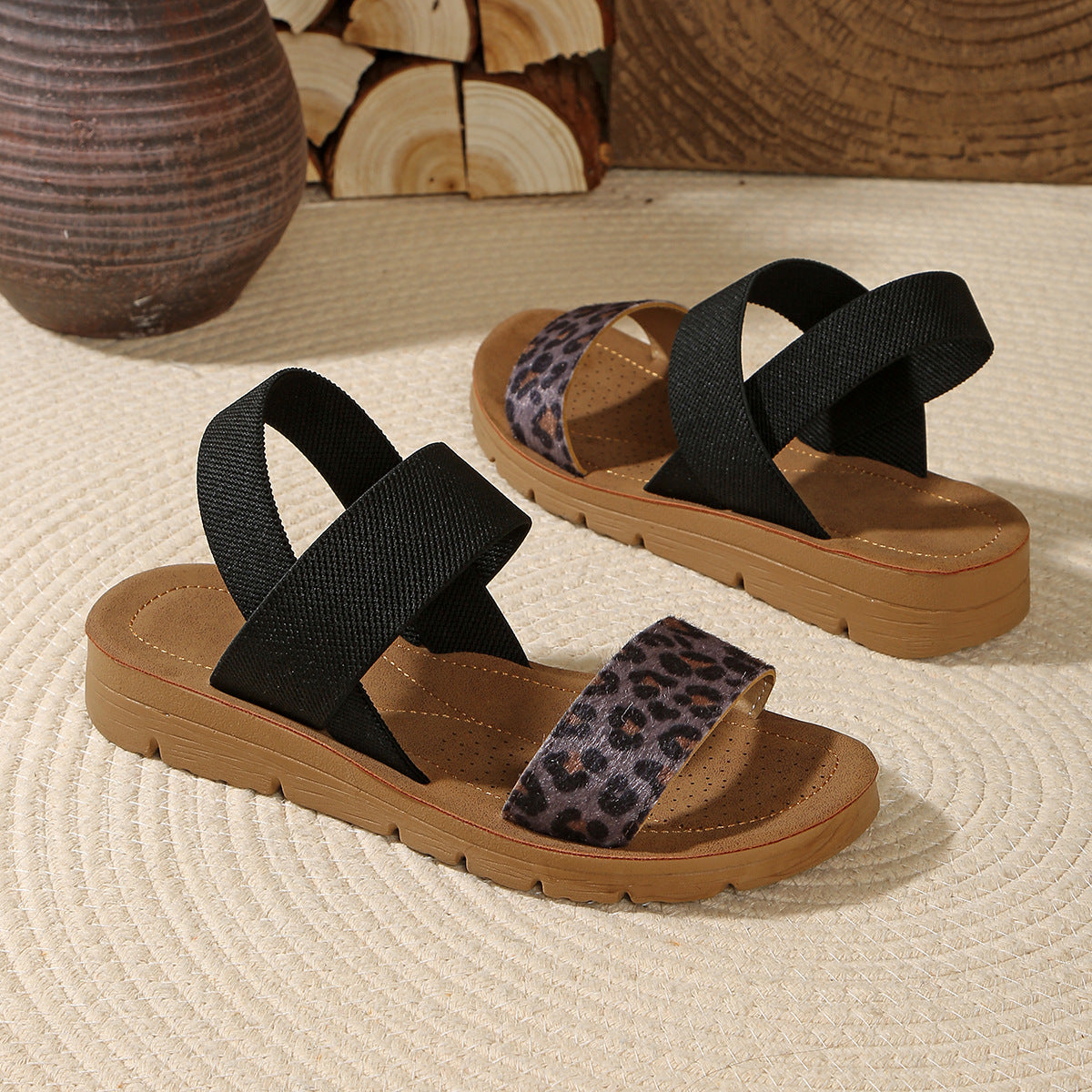 Pair of sandals with black and leopard print straps on a textured surface.