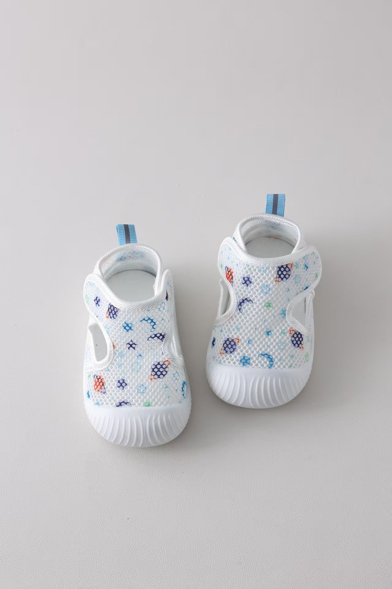Pair of white baby shoes with colorful patterns on a light gray background