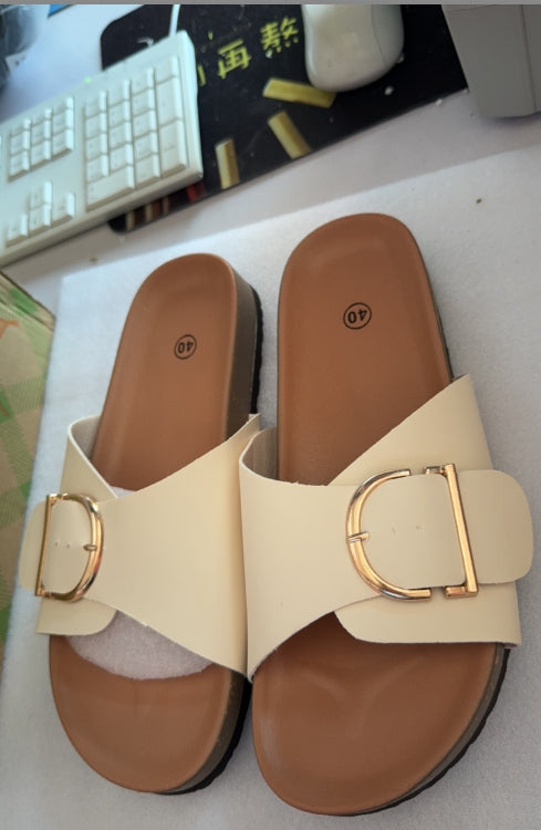 Beige sandals with gold buckles on a desk with a keyboard and mouse in the background.