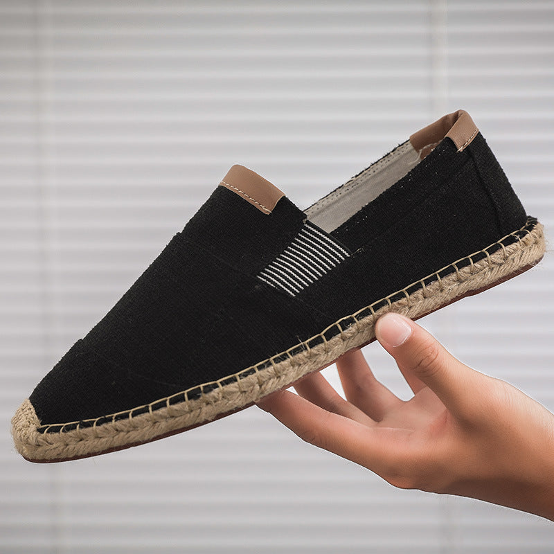 Black espadrille shoe held by a hand against a neutral background