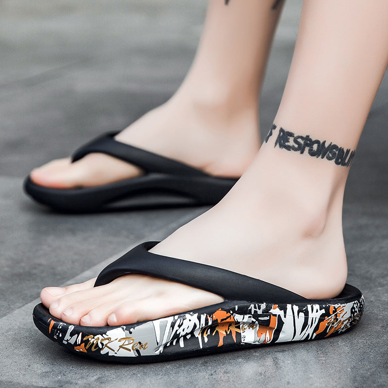 Black flip-flops with a colorful pattern worn by a person on a gray surface