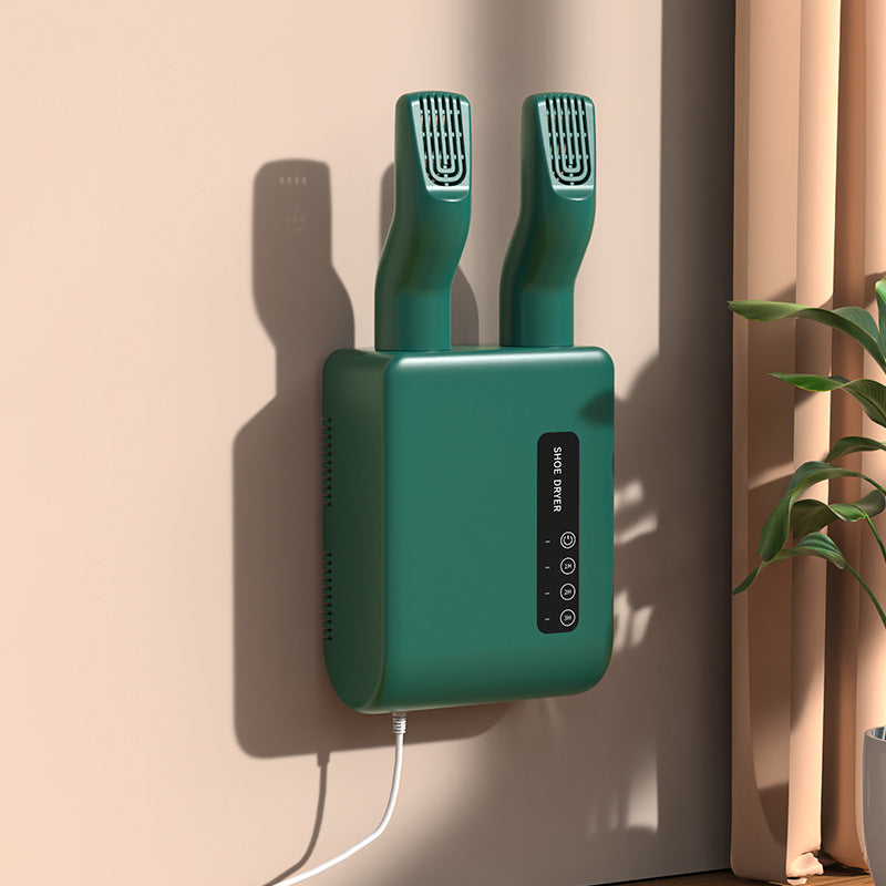 Green wall-mounted device with two nozzles on a beige wall.
