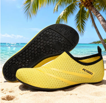 Yellow and black water shoes on a sandy beach with palm trees and blue sky.