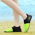 Black and green beach shoes on a person's feet with a blurred beach background