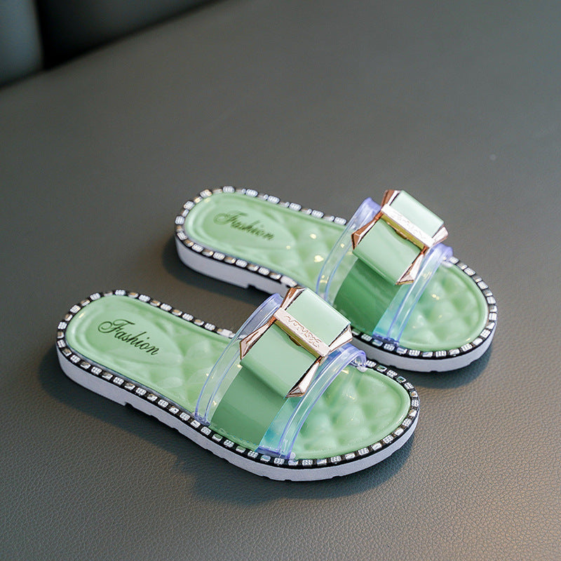 Pair of green slides with decorative straps on a gray surface