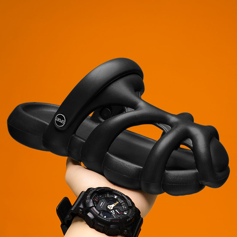 Black sandals held by a hand wearing a black watch against an orange background