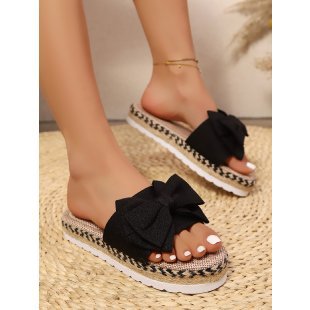 Black sandals with bow details worn by a person on a textured surface