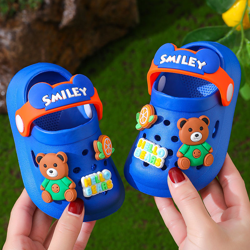 Blue children's sandals with teddy bear design held by a person against a natural background