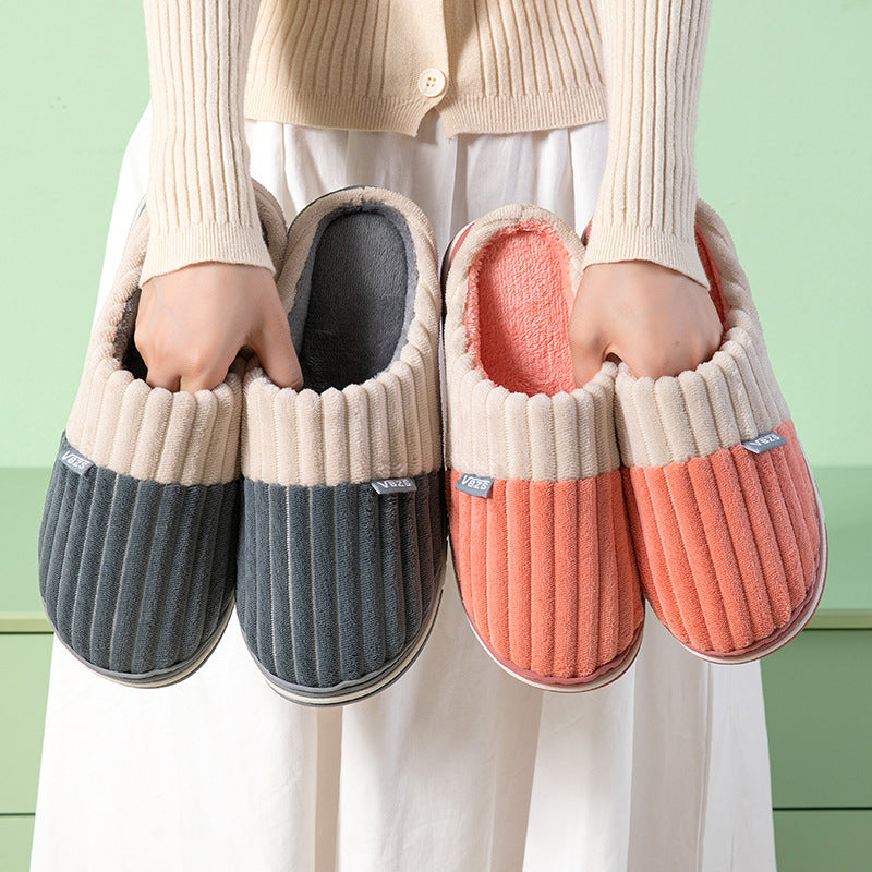 Two pairs of slippers, one gray and one pink, held by a person against a green background.