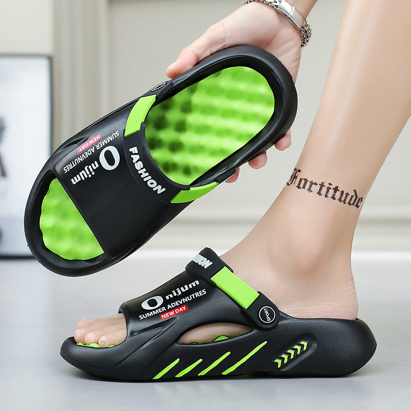 Black and green sandals held by a hand with a tattoo on a neutral background