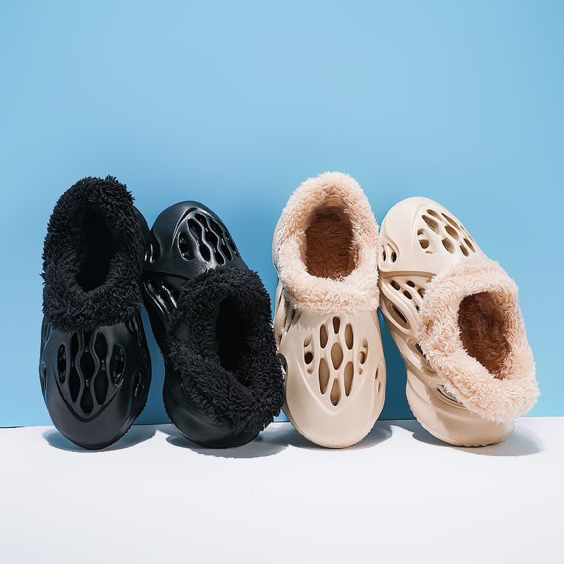 Black and beige slippers with fuzzy interior on a light blue background