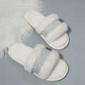 White slippers with fluffy texture and silver glittery straps on a gray background