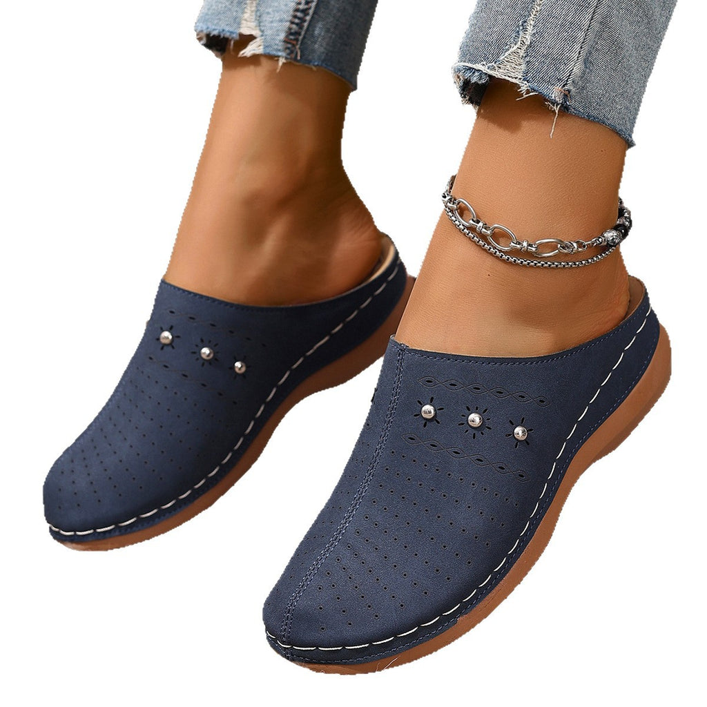 Navy blue clogs with pearl embellishments worn with denim jeans on a white background
