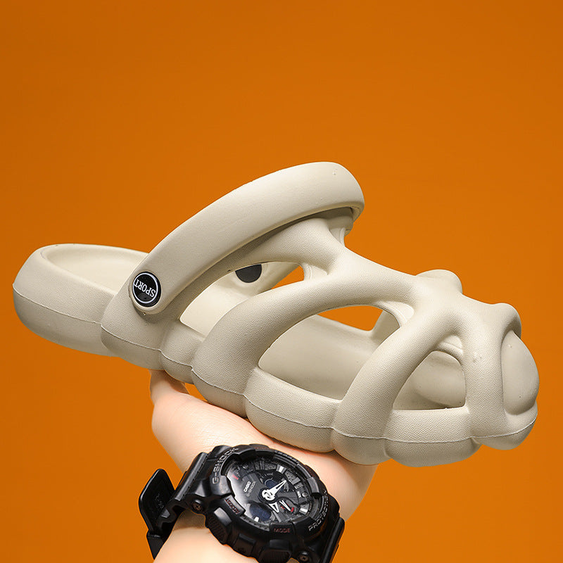 Beige sandals with a brand logo held by a hand wearing a black watch against an orange background