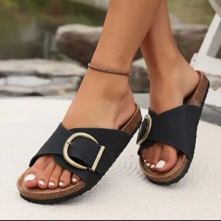 Black sandals with brown soles worn by a person on a blurred outdoor background