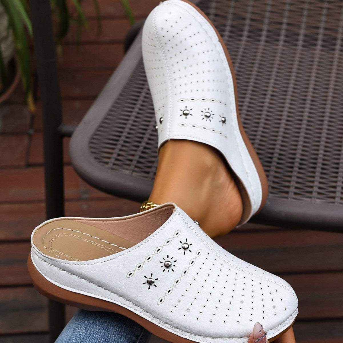 White clogs with brown soles worn by a person sitting on a chair.