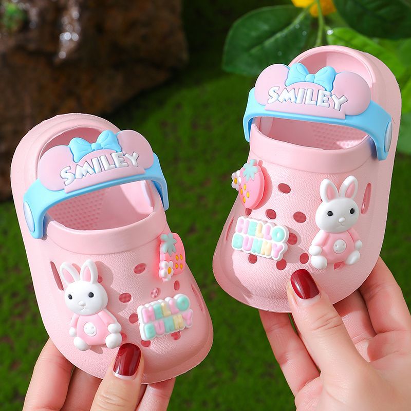 Pink children's sandals with bunny design held by a hand against a green background