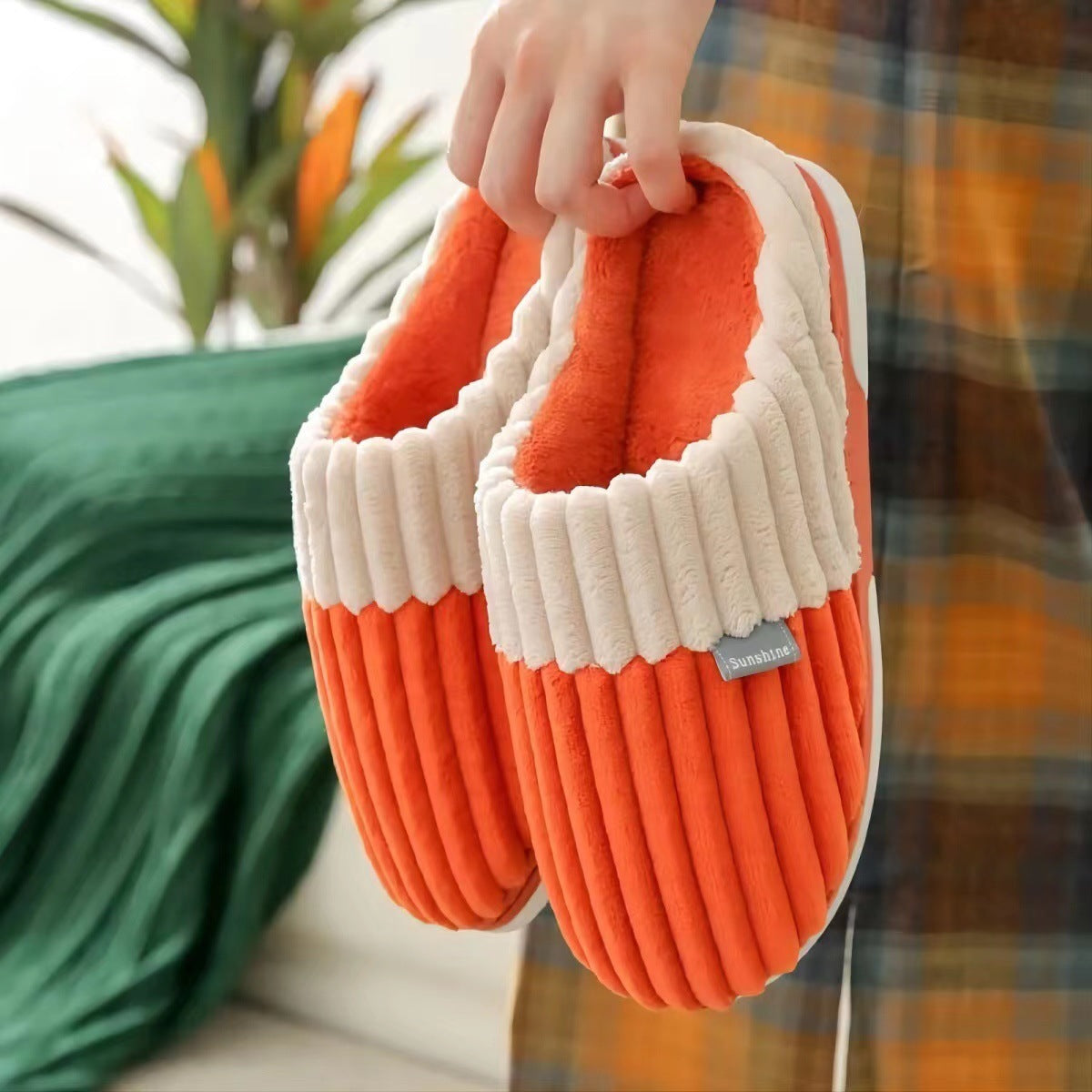 Orange and white slippers held by a person with a blurred indoor background