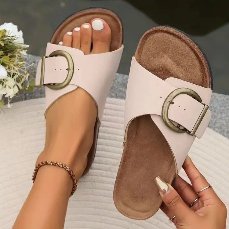 White sandals with a gold buckle held by a person on a blurred background