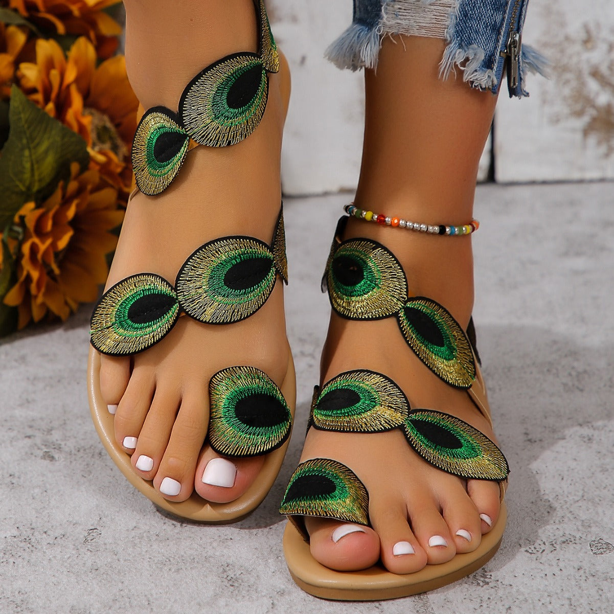 Beige sandals with peacock feather designs worn by a person on a light background