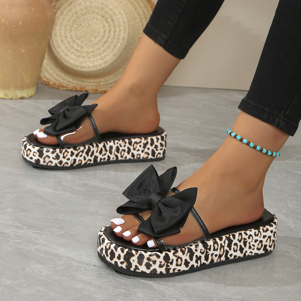 Black sandals with leopard print platform sole worn by a person on a gray floor.